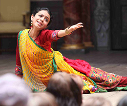 An actress wearing a red and yellow sari on stage performing in the production All's Well That Ends Well in the language Gujarati at Shakespeare's Globe Theatre, London